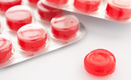 Packets of red coloured throat lozenges on a white background. Adobe